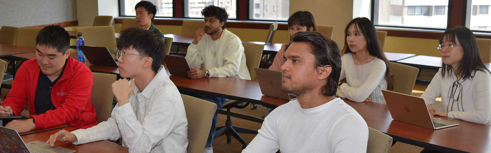 students sit in classroom and pay attention with their laptops open