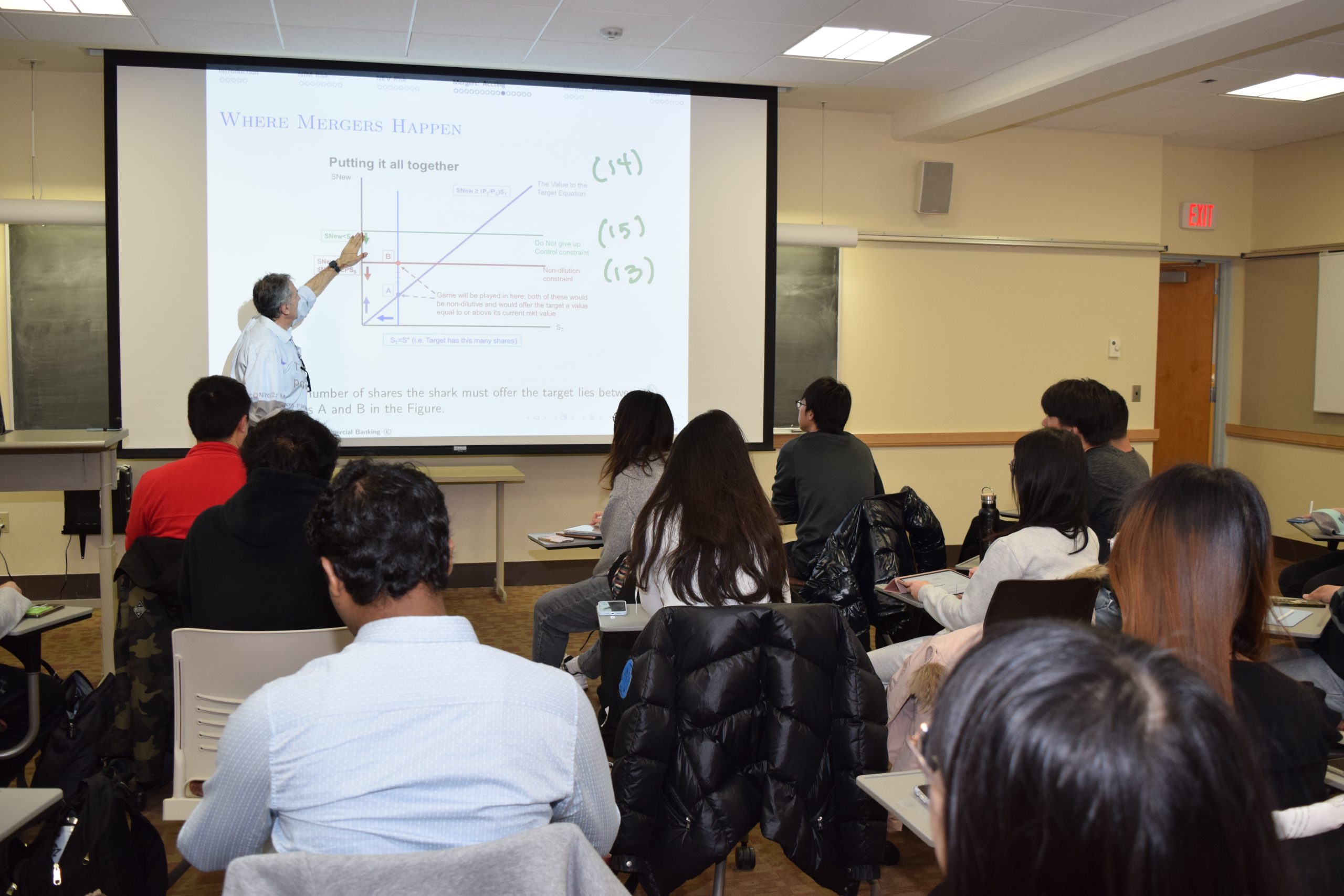 graduate students sit in a classroom, listen and take notes as the professor instructs