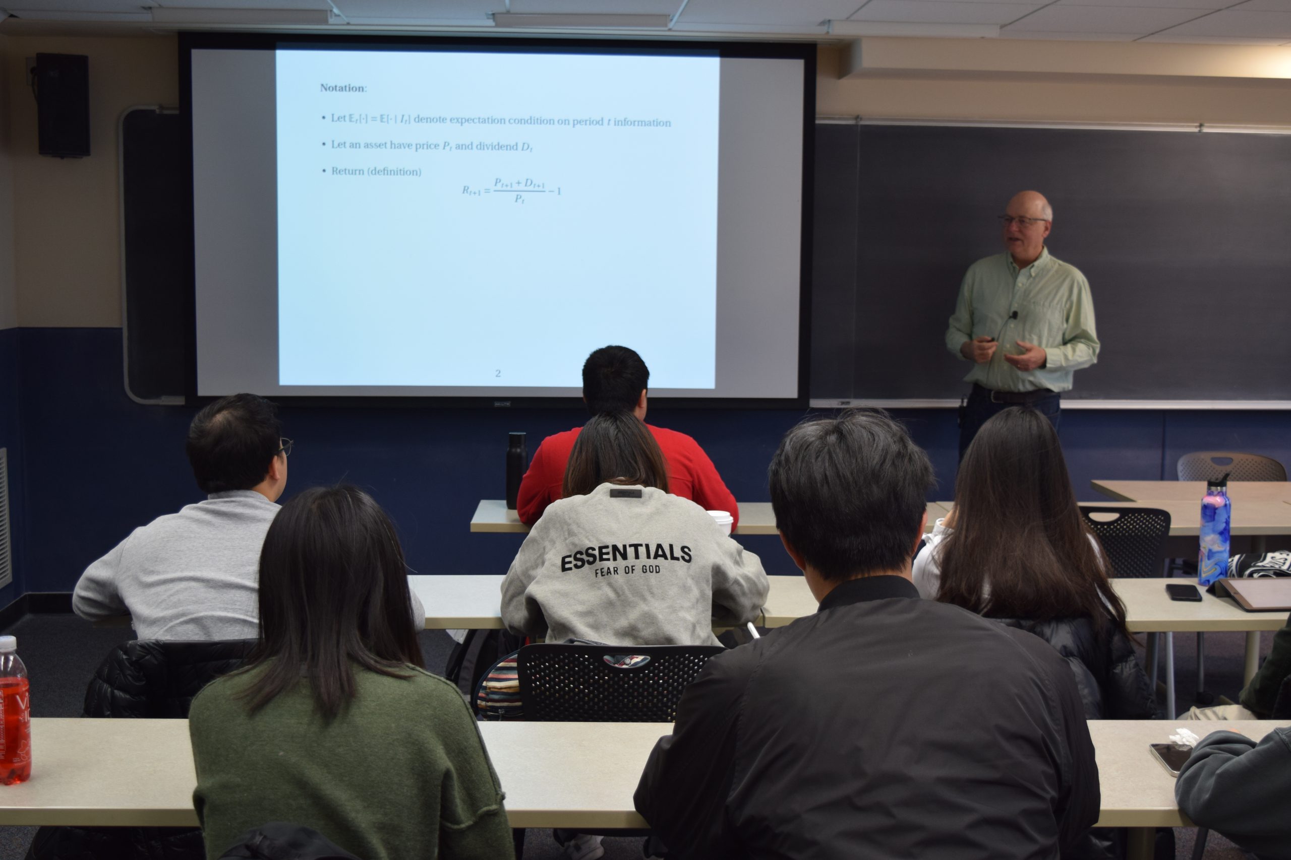 graduate students sit in a classroom, listen and take notes as the professor instructs