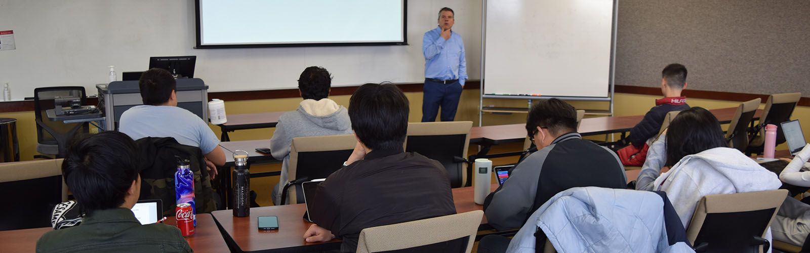 graduate students sit in a classroom, listen and take notes as the professor instructs